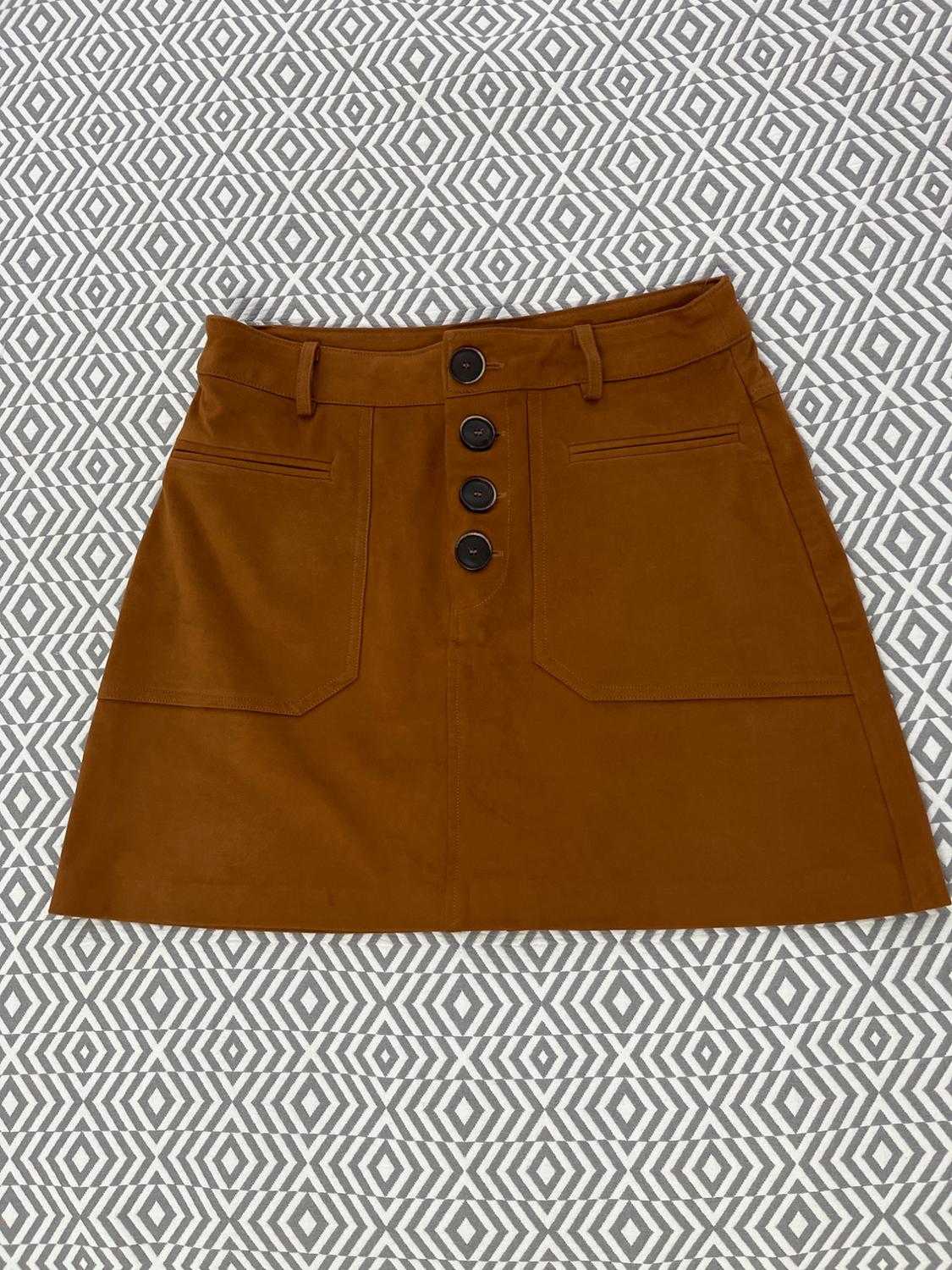Brown skirt with black buttons and front pockets on a white and grey geometric background.