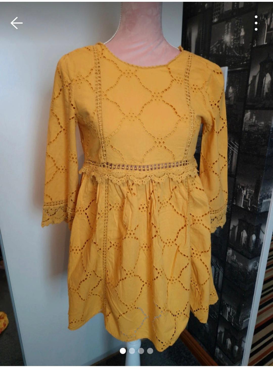 Yellow dress with openwork embroidery and long sleeves on a mannequin, background with black and white images of buildings.