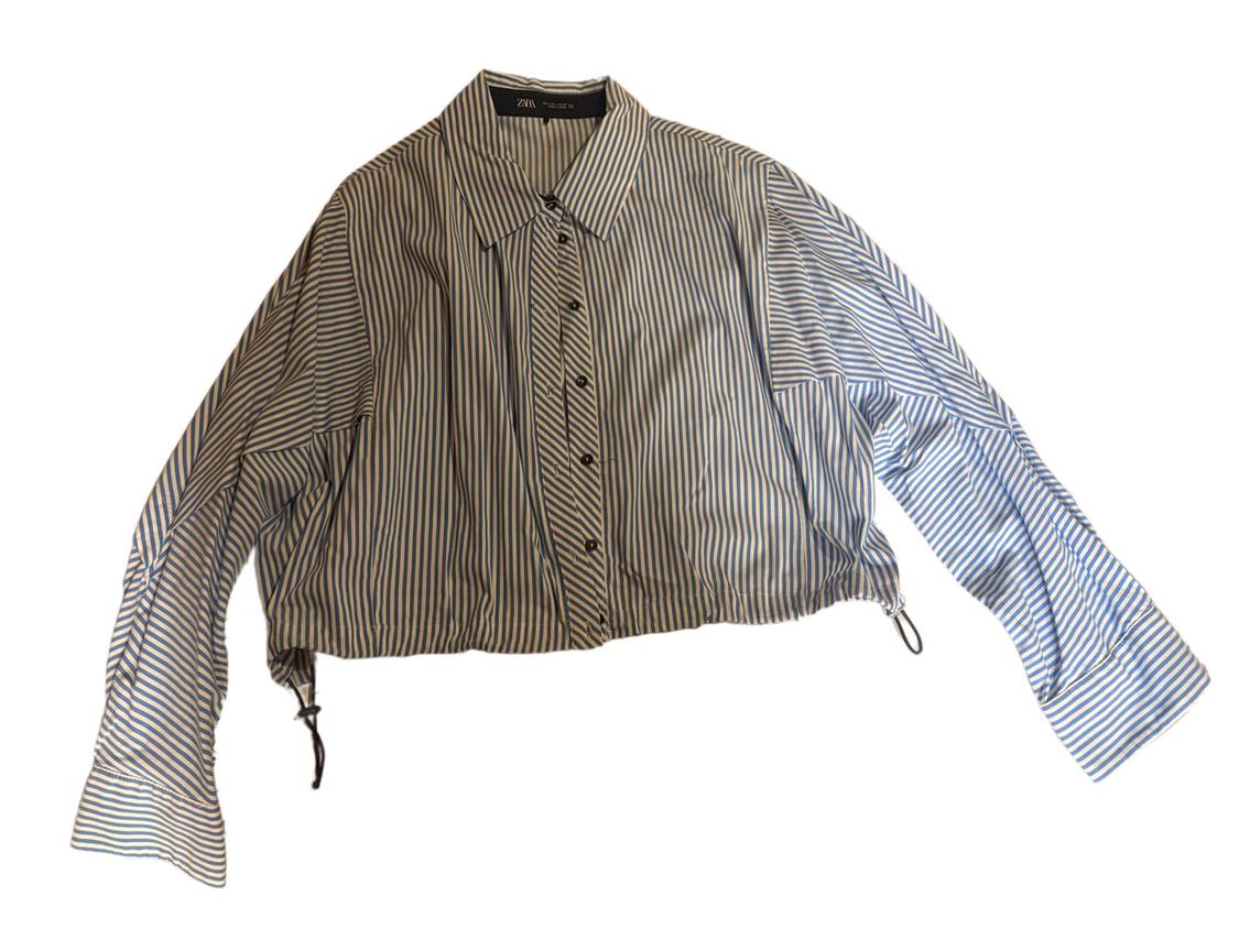 Blue and white striped shirt with black buttons and long sleeves. Cropped, loose-fitting design with a classic collar.