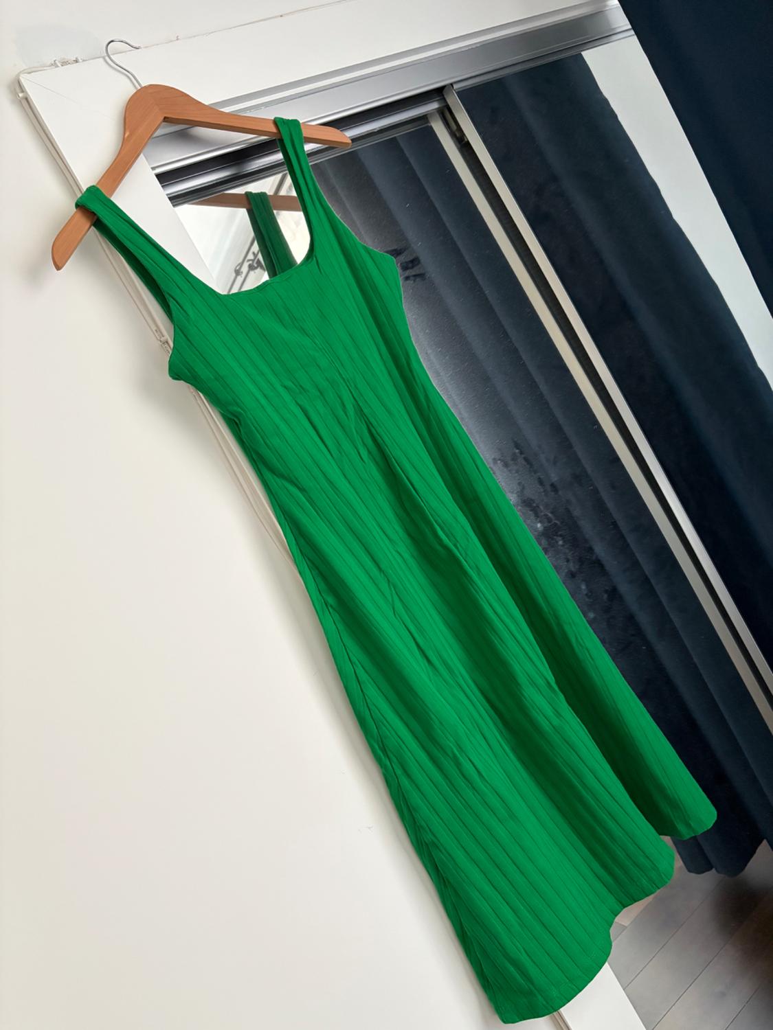 Green sleeveless dress hanging on a wooden hanger over the mirrored door of a wardrobe. Reflection of a dark curtain.