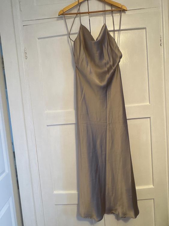 Beige satin dress with spaghetti straps, hanging on a wooden hanger in front of a white door.