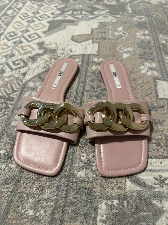 Pink sandals with gold chain detail on a geometric design rug in beige and gray tones.