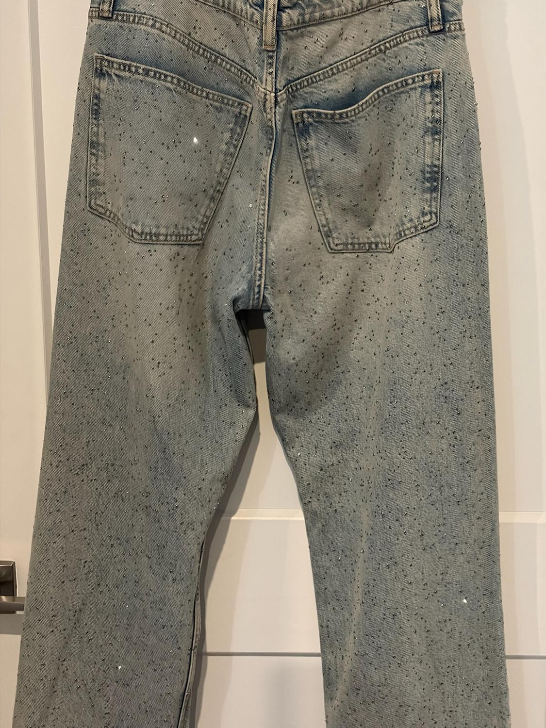 Light-blue jeans seen from behind, adorned with small sparkles all over, hanging in front of a white door.