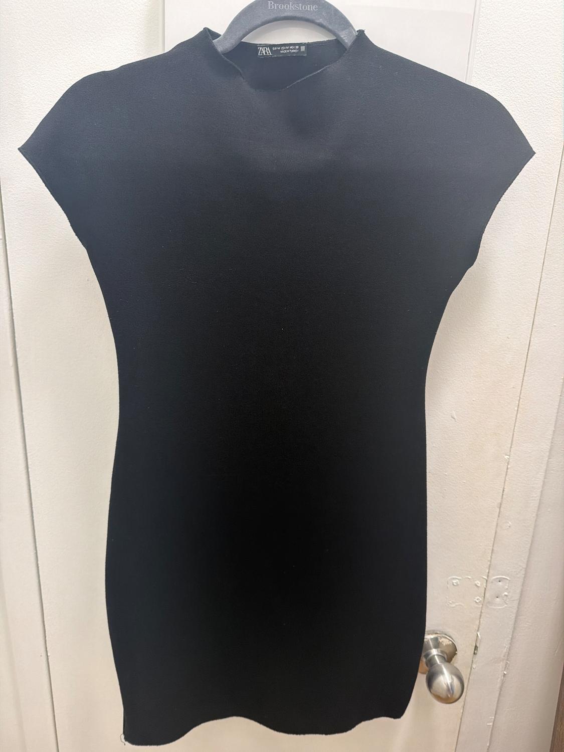 Black turtleneck dress hanging on a white door. “Brookstone” text on the hanger and ZARA on the tag.