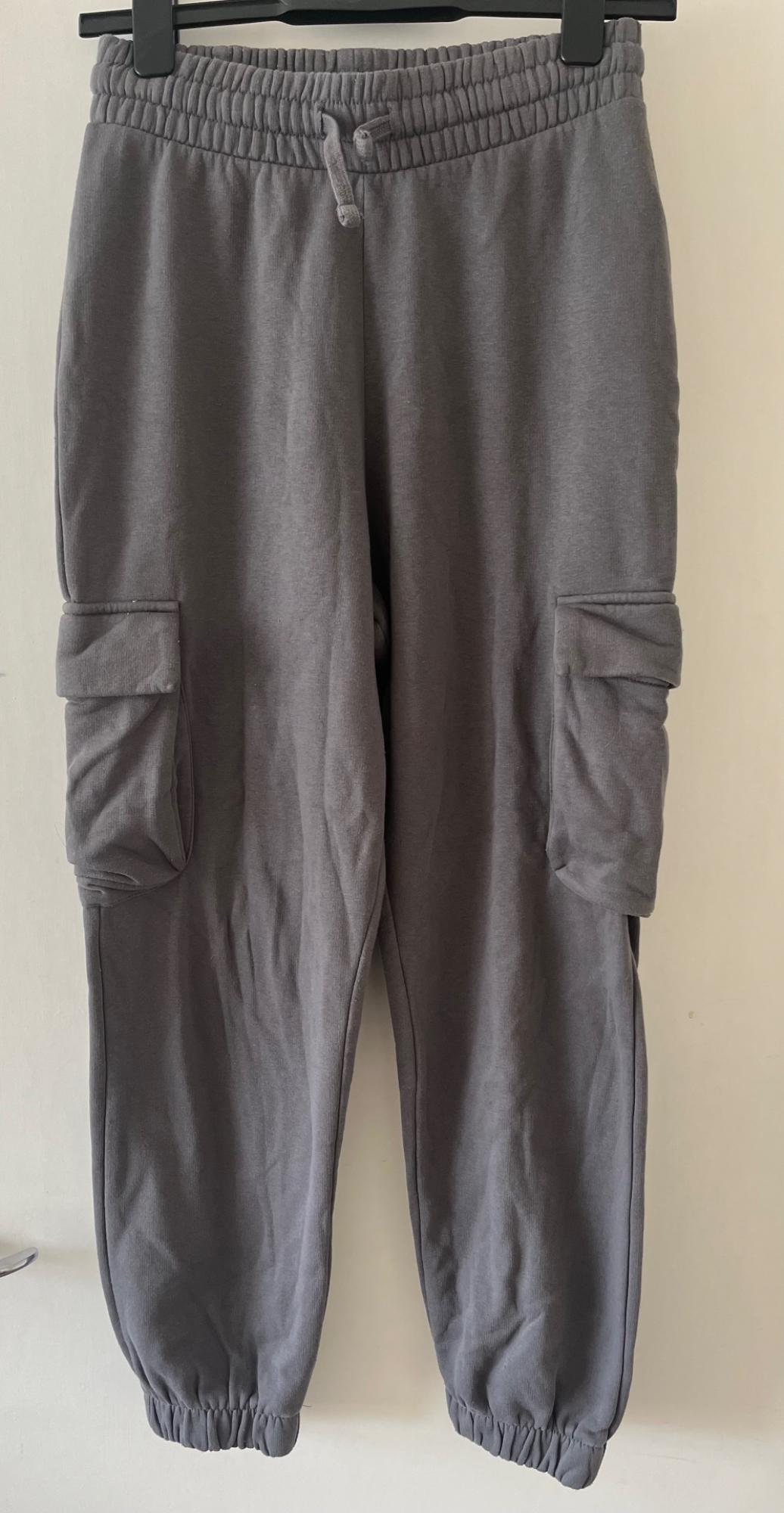 Grey cargo-style joggers on a hanger against a white background. They feature an elasticated waistband with a drawstring, side pockets, and elasticated cuffs.