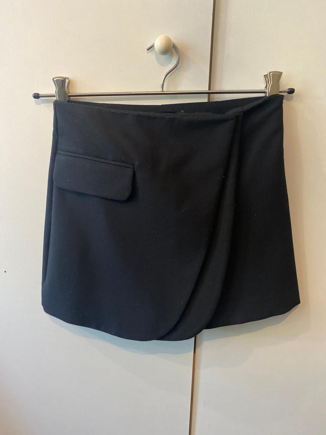 Black skirt hanging on a metal hanger, with a side pocket, against a white door background.