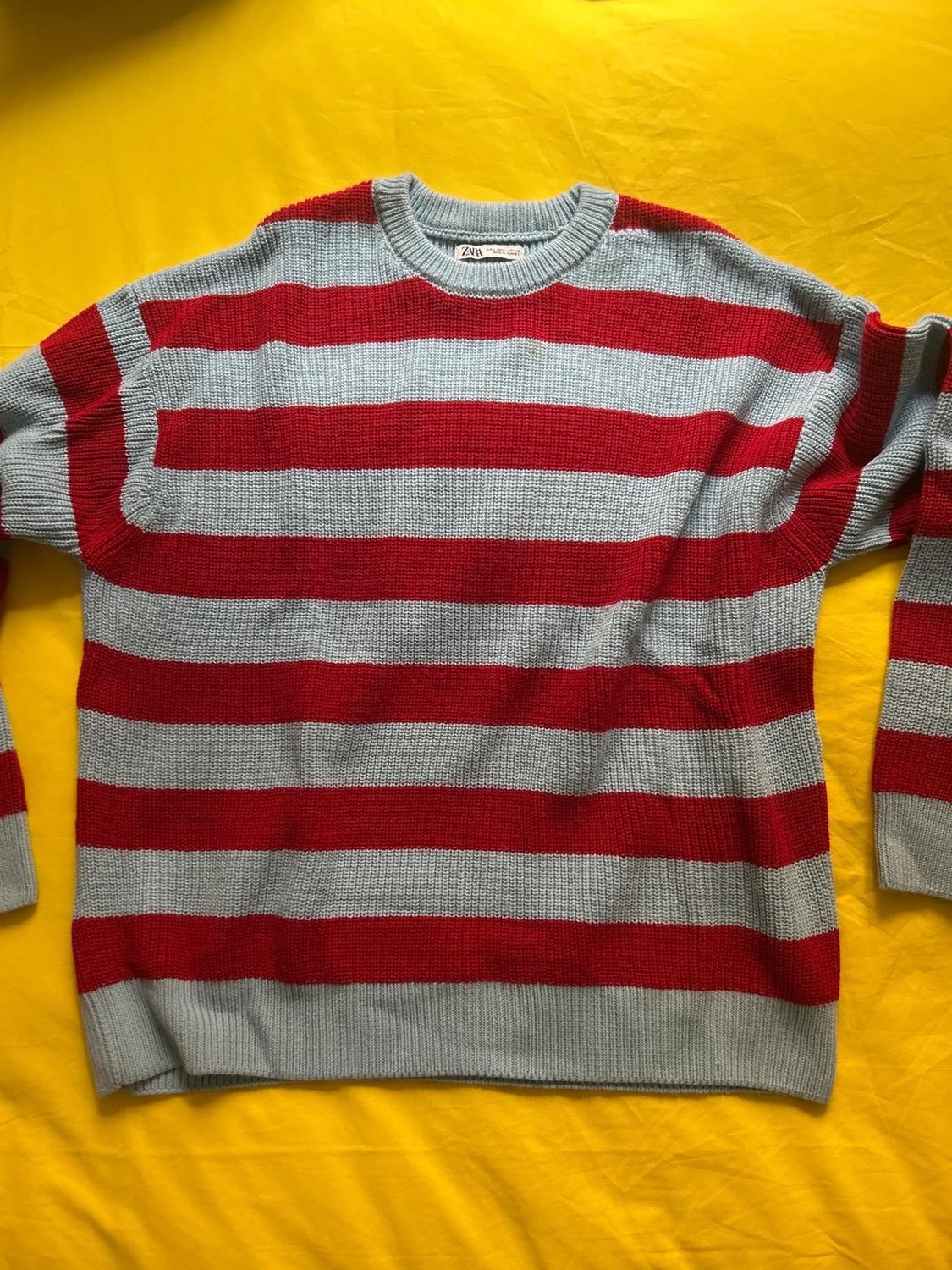 Red and grey horizontal striped jumper on a yellow background. Visible label on the collar.