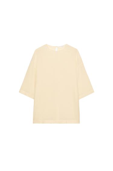 Front view of a butter-coloured blouse, short wide sleeves, round neck, regular hem with side slits and back closure.