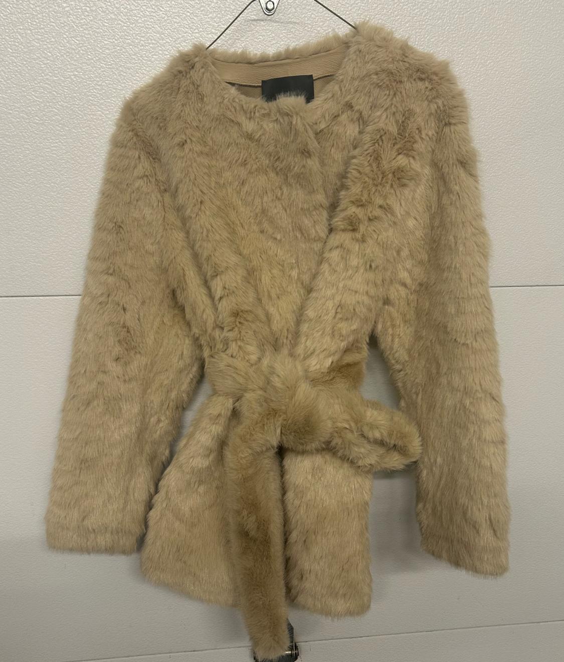 Beige teddy coat hanging on a white wall, with belt tied at the front and a round neck.