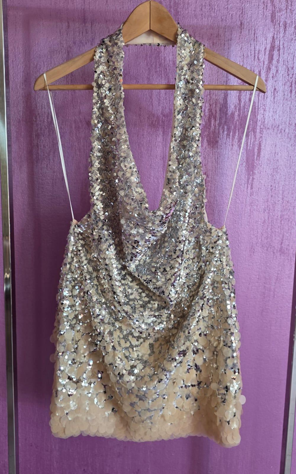 Short, silver sequinned dress hanging on a wooden coat hanger, against a purple wall backdrop.