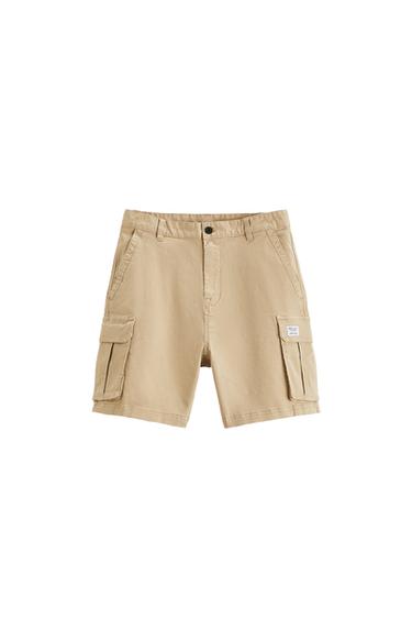 Elastic waistband shorts. Front pockets and back flap pockets. Flap patch pockets at legs. Front zip and button closure.