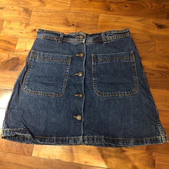 Front view of a blue denim skirt with front pockets and a central button closure.
