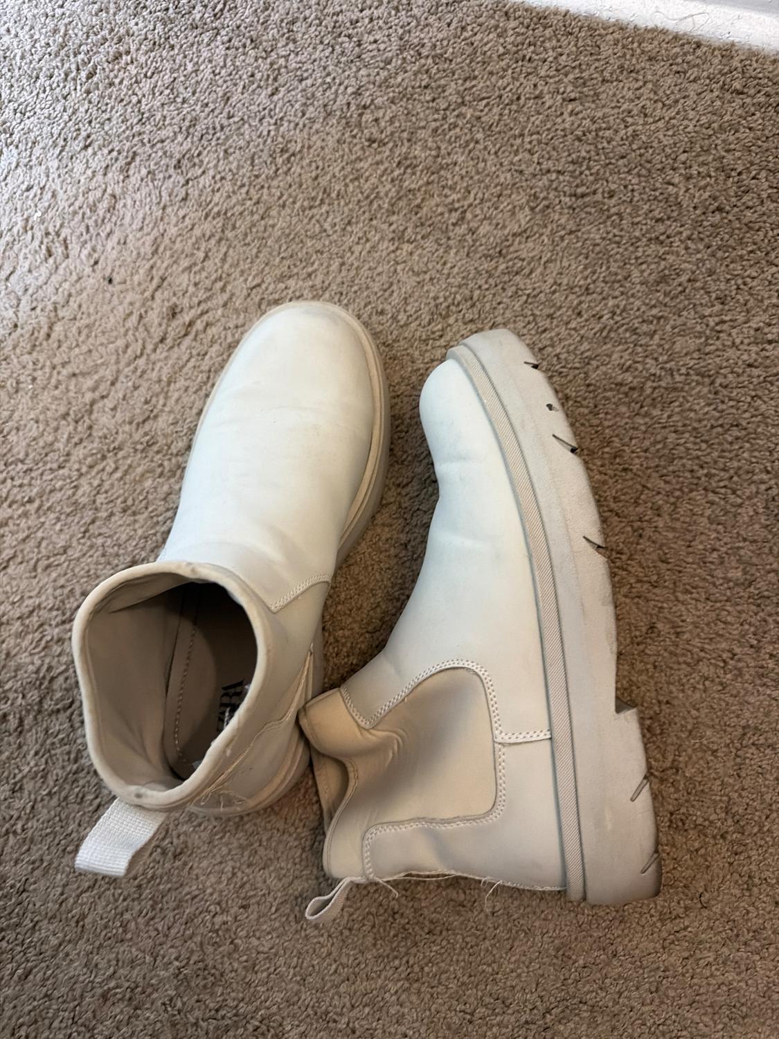 White chunky-soled boots on a beige carpet. One boot is standing upright and the other is lying down, showing its interior.