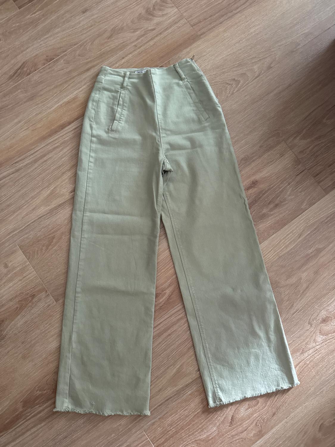 Light green, high-waisted, wide-leg trousers with a frayed hem on a wooden floor. ZARA label visible on the waistband.