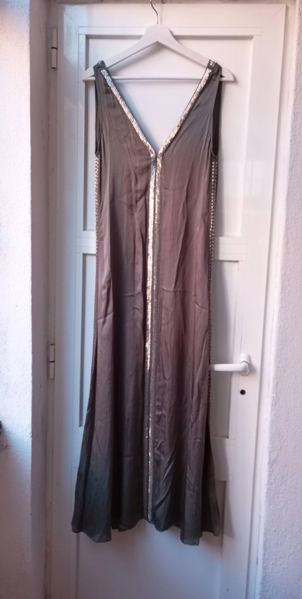 Long grey dress with sparkly detailing on the hem, hanging on a white hanger over a white door.