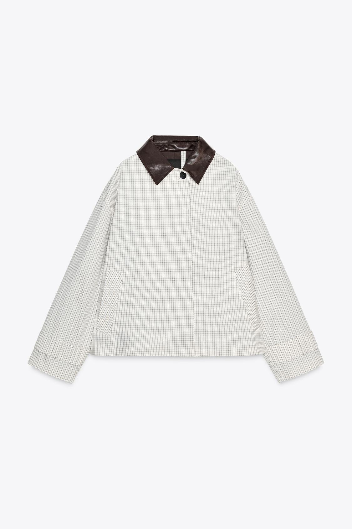 Sprednji pogled na črno-bel kratek trenč plašč s kontrastnim rjavim ovratnikom, dolgimi rokavi, sprednjimi žepi in skritim zapiranjem na gumbe.