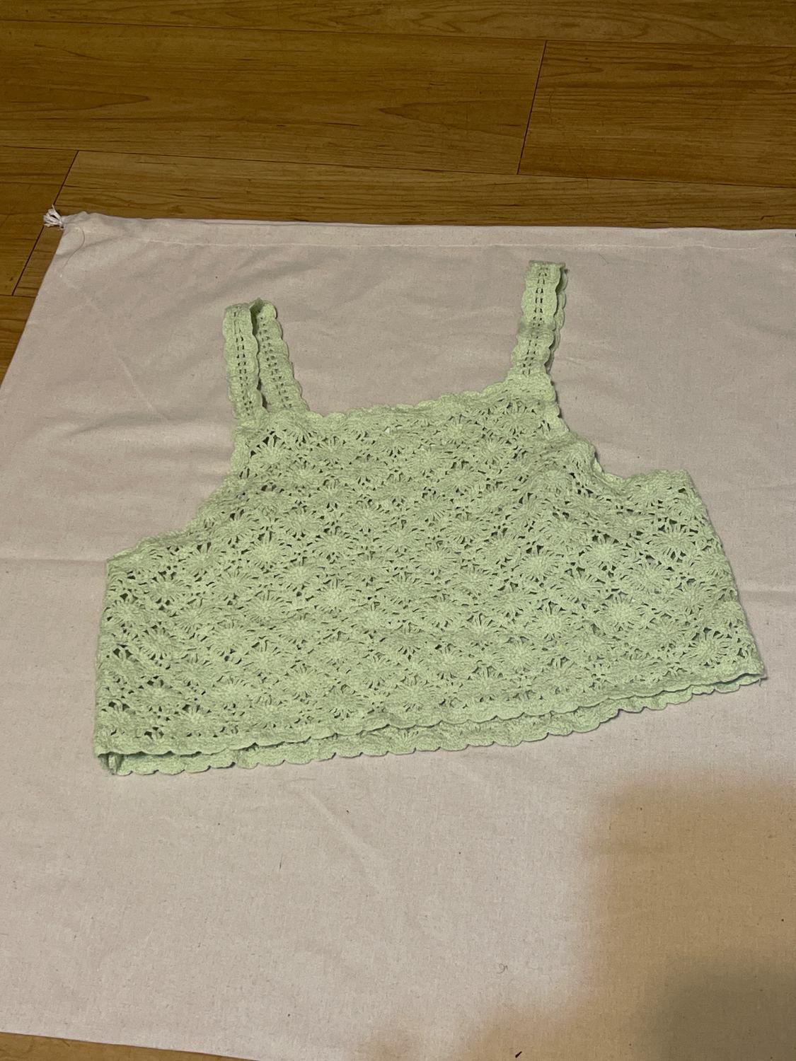 Light green crochet top with wide straps, on white fabric and wooden floor.