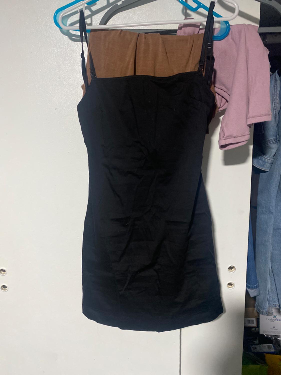 Sleeveless black dress hanging on a blue and white hanger, against a white door background. Next to it, a pink garment.