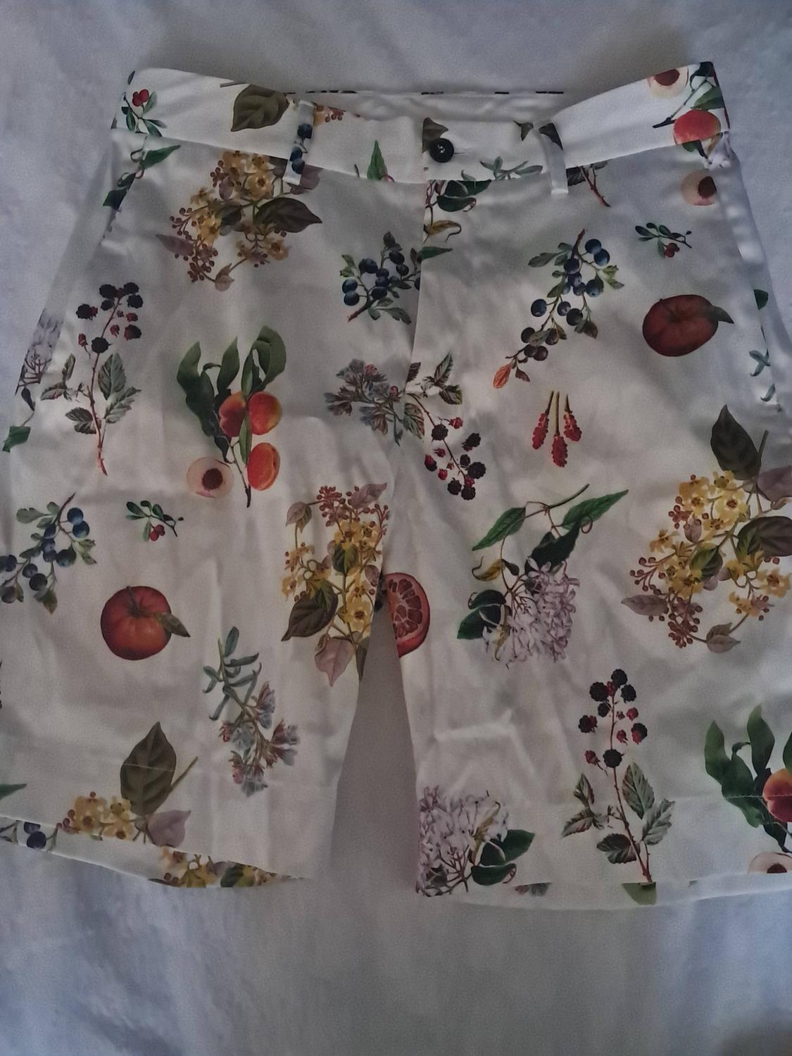 White shorts with a botanical fruit and floral print. Casual design with a button and belt loops, photographed against a white background.