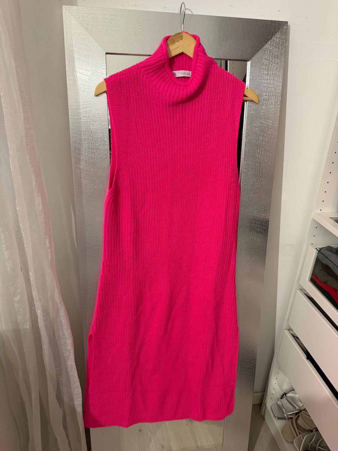 Fuchsia sleeveless dress hanging on a silver-framed mirror. Background with a white curtain and a shelving unit with clothes.