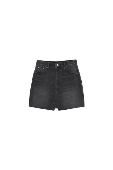 Black denim mini skirt with a washed-out finish against a white background. High-waisted design with pockets, button fastening, and a front hem slit.
