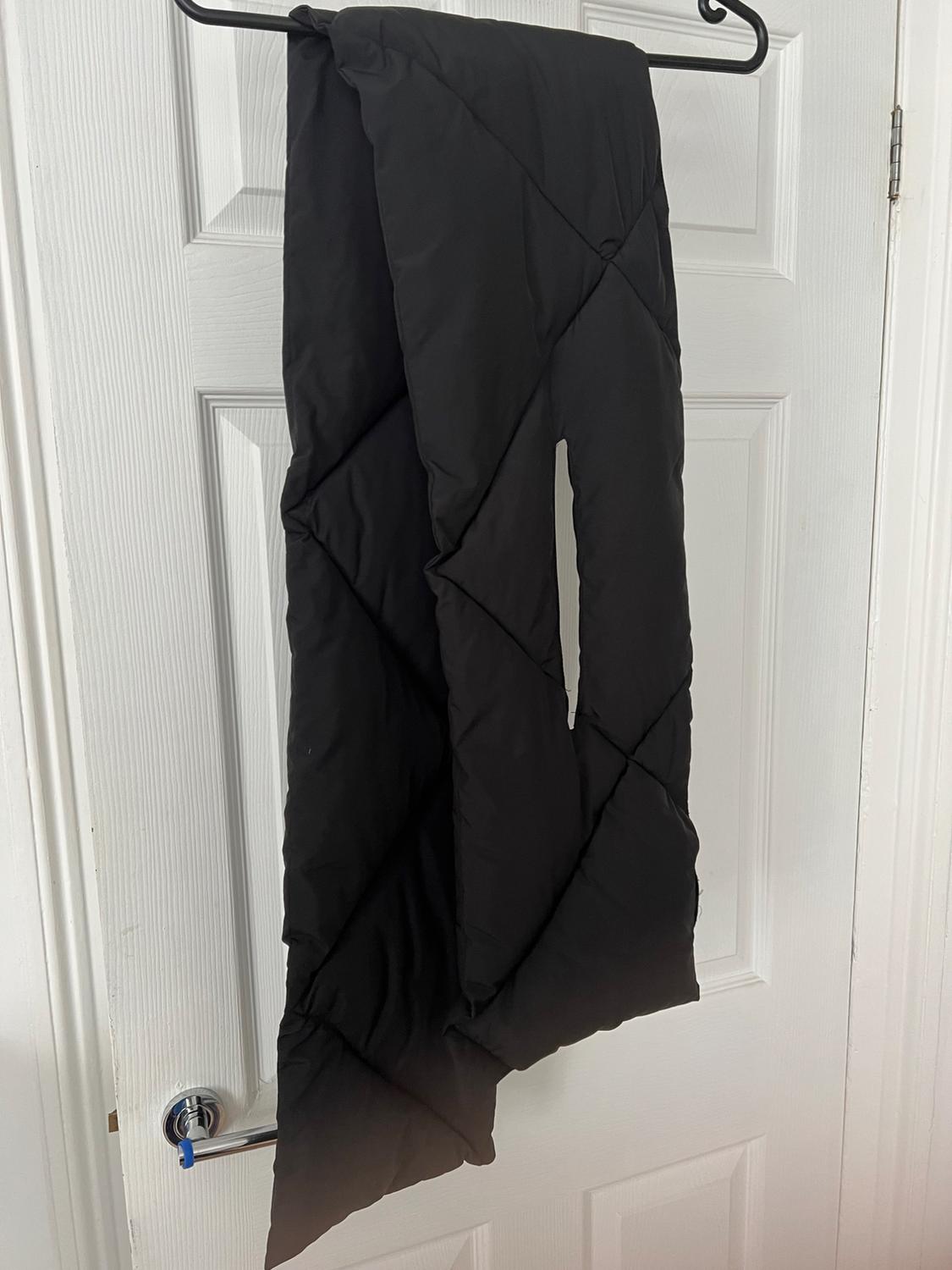 Black quilted diamond-patterned scarf with a slit, hanging on a coat hook on a white door.