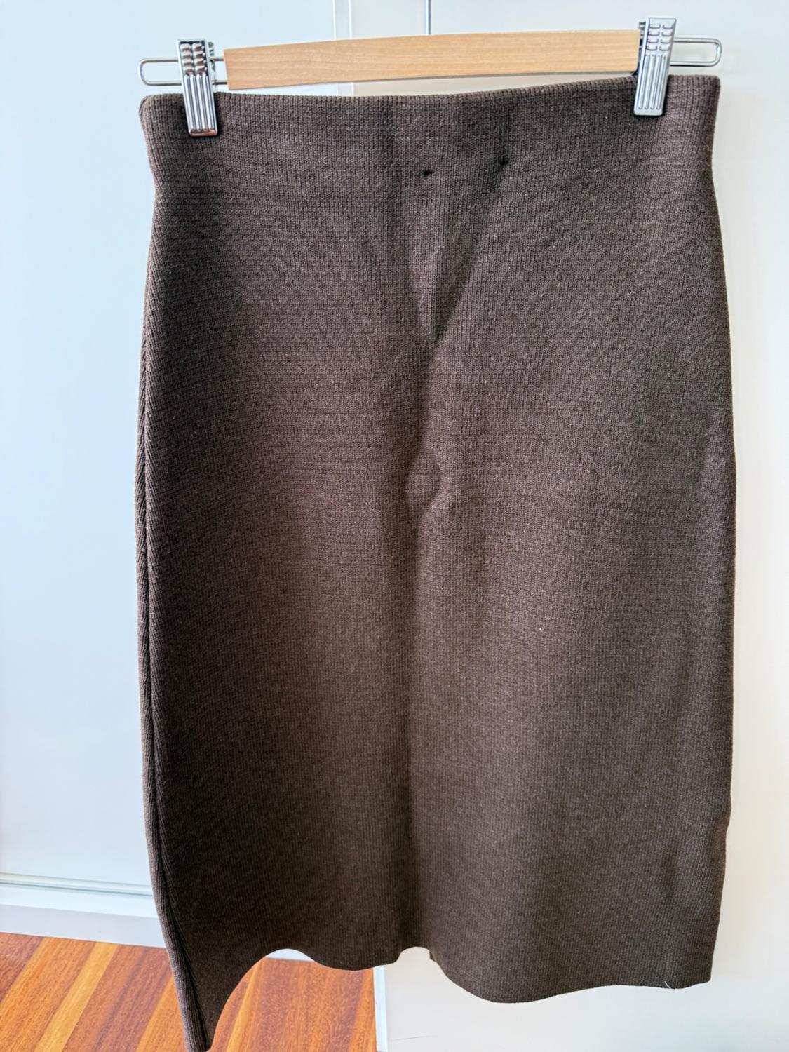 Brown knitted skirt hanging on a wooden hanger, white background and wooden floor.