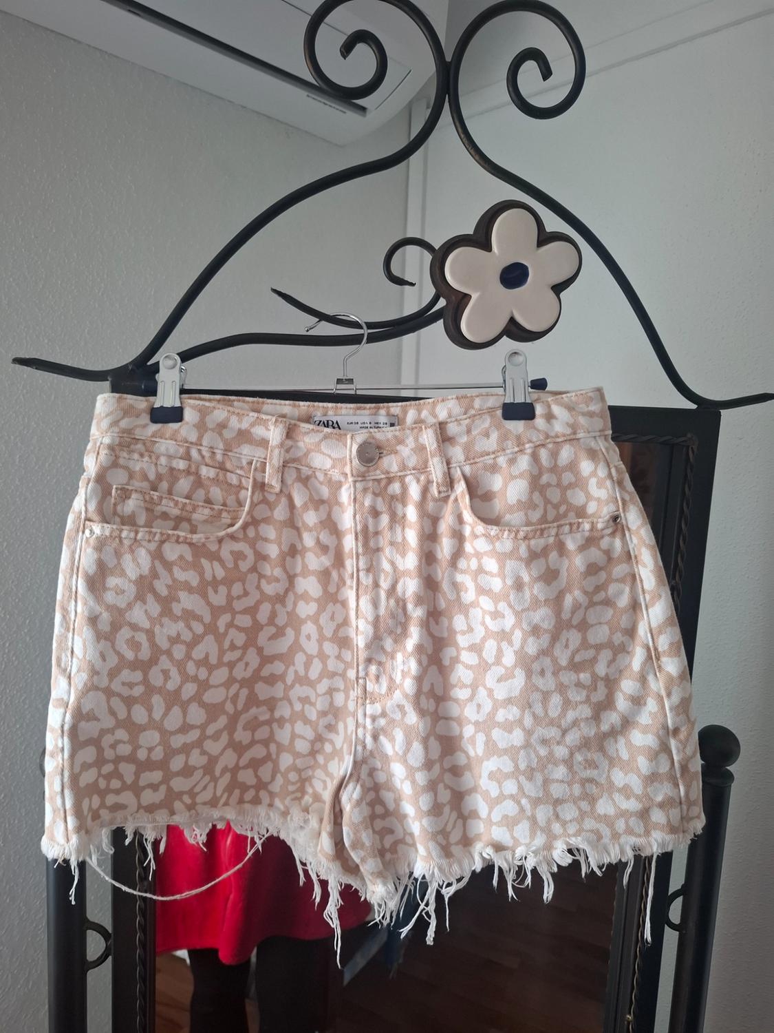 Beige and white animal print denim shorts, hanging on a decorative hanger with a flower on a mirror.