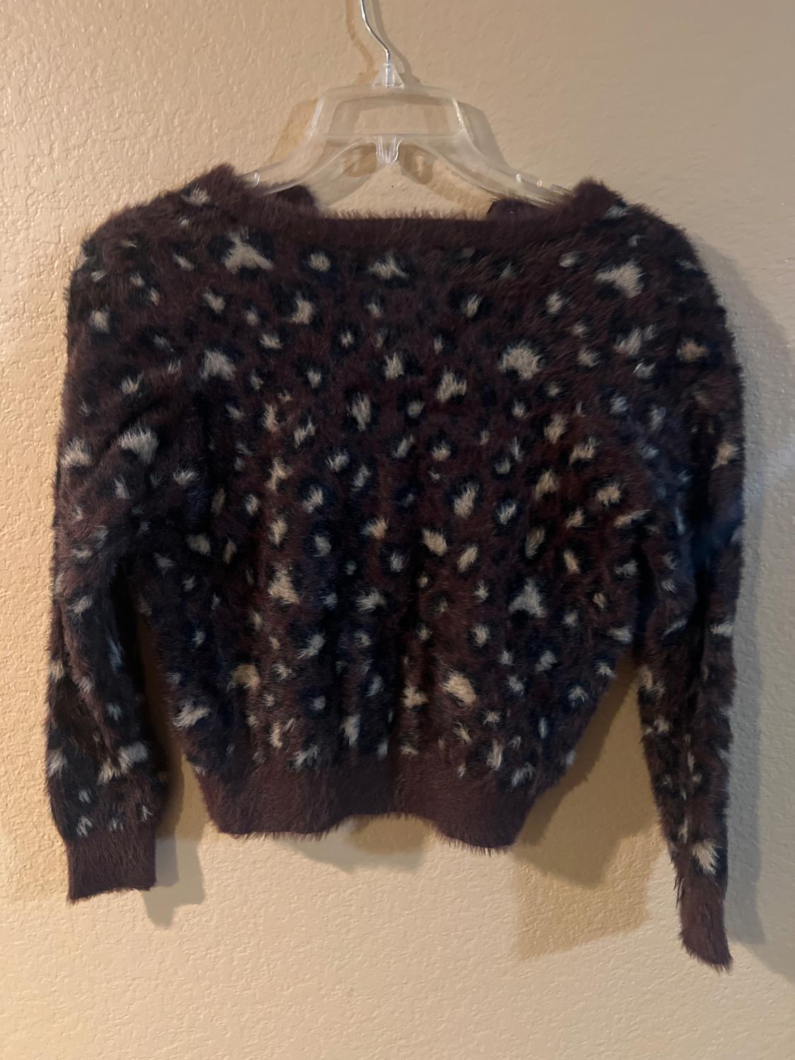 Fuzzy knit sweater with dark and light spot print, hanging on a clear hanger against a beige wall.