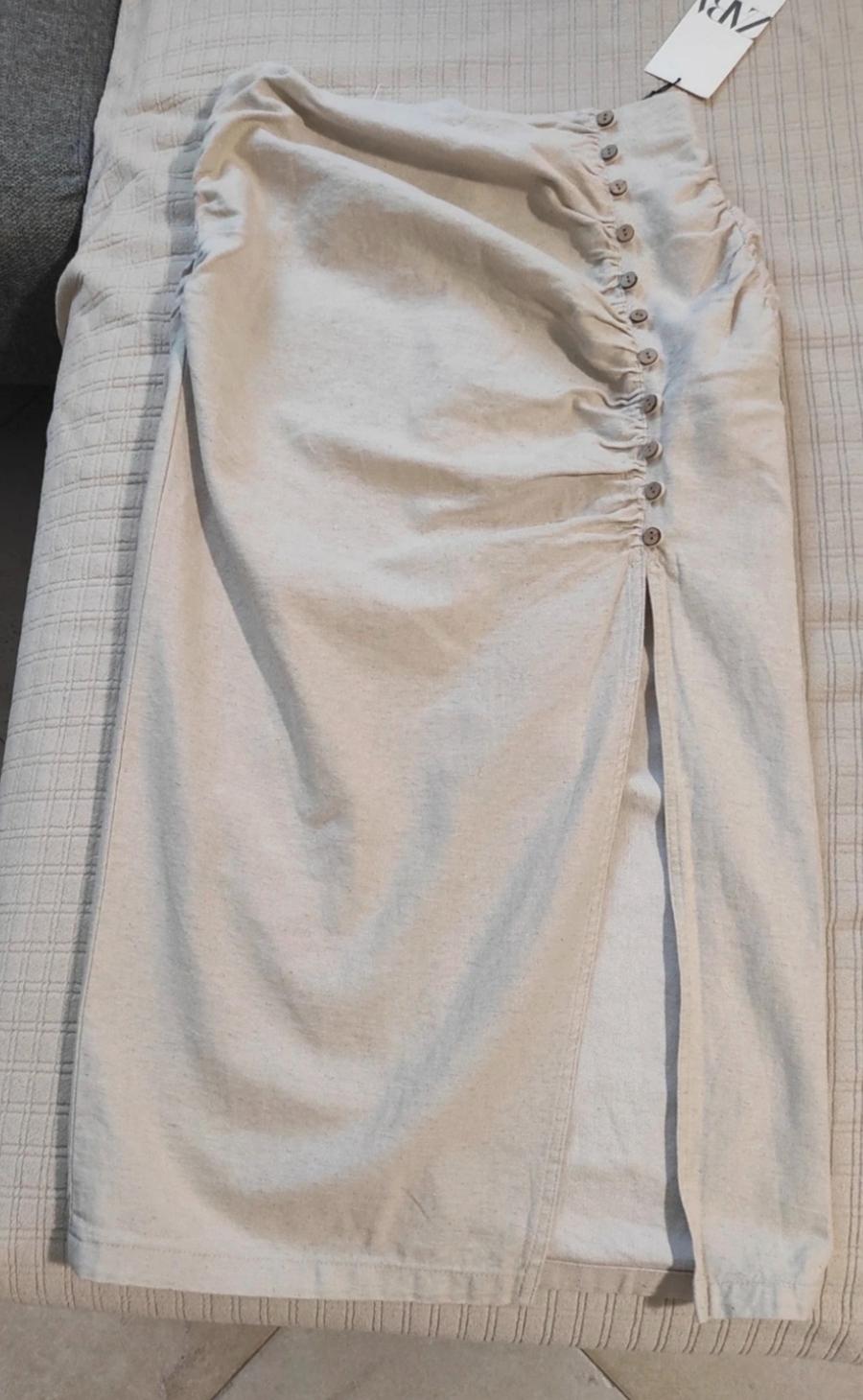 Beige skirt with side slit, ruched detail and buttons on one side, on a light textured surface. Label visible.