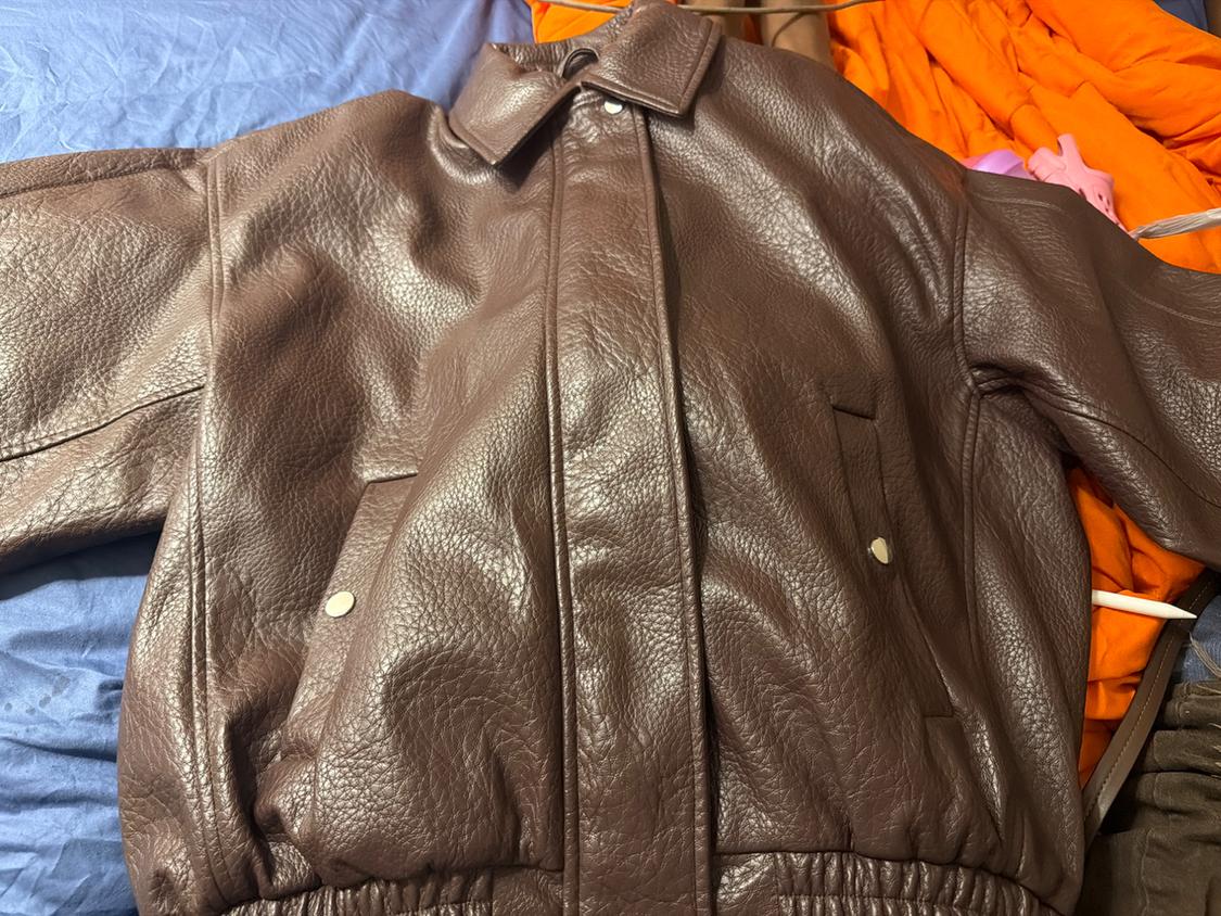 Textured brown bomber jacket on an unmade bed with blue and orange sheets. Relaxed and casual atmosphere.