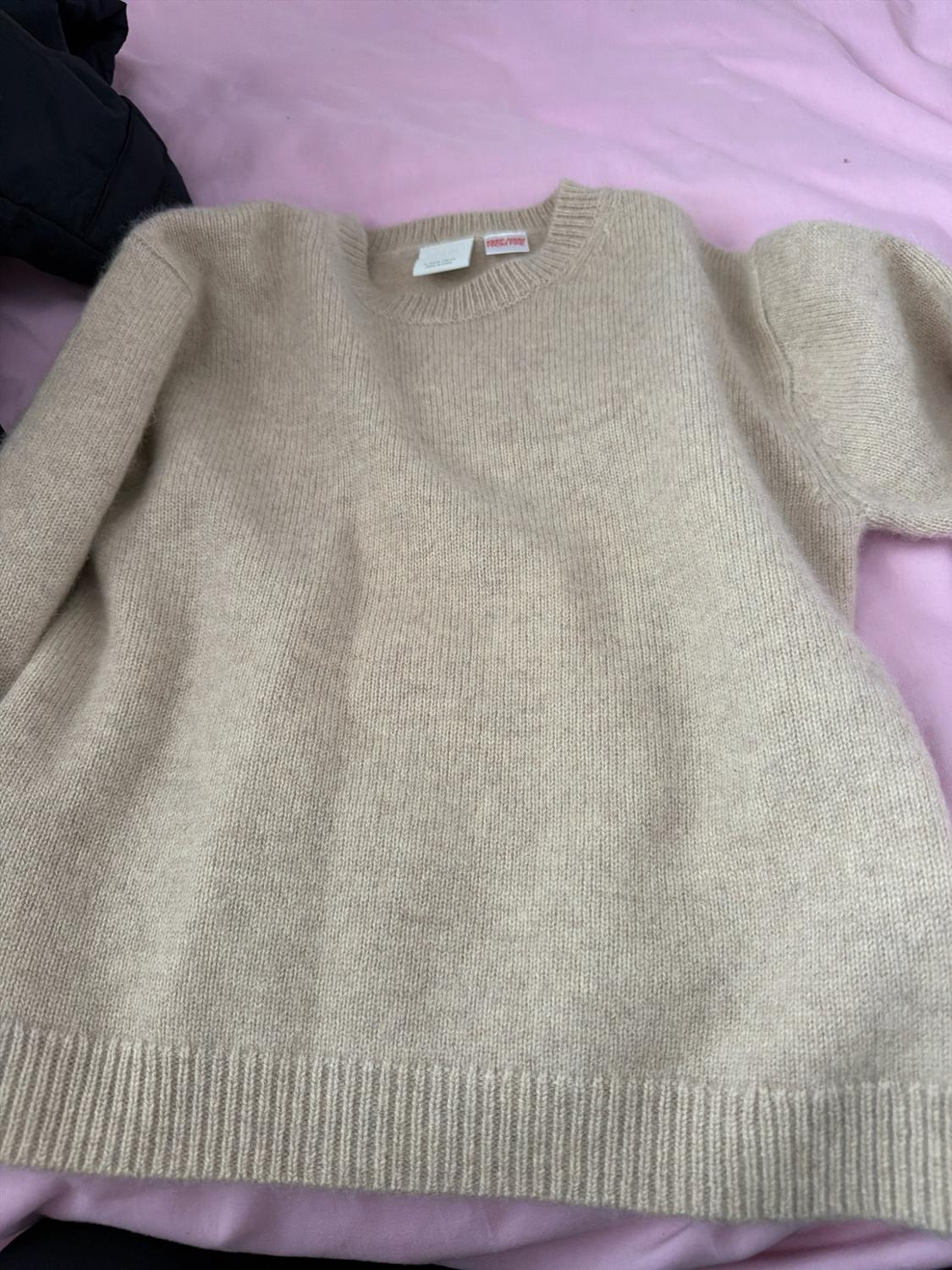 Beige knitted jumper with a crew neck and ribbed trims, laid out on a crumpled pink fabric.