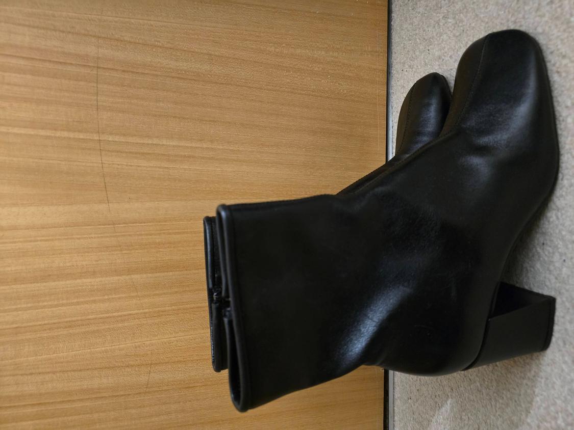 Black leather boots with a block heel on a light wooden background and a beige rug.
