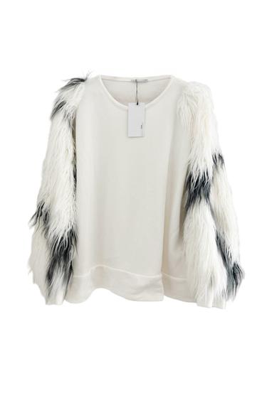 White crewneck sweatshirt with long sleeves made of white and black faux fur. Visible label on the neck. White background.