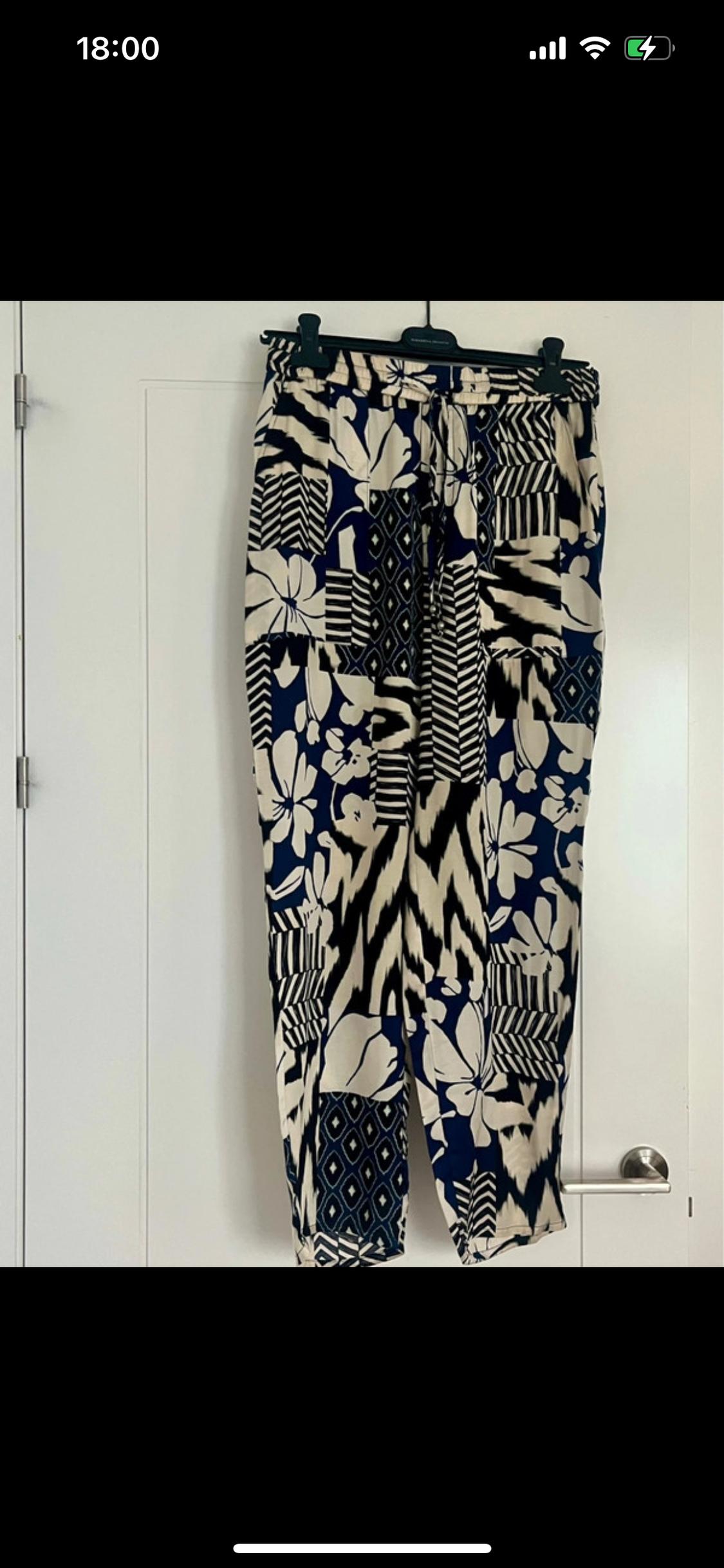 Trousers hanging with a floral and geometric print in white and navy blue, over a white door. Time on screen: 18:00.