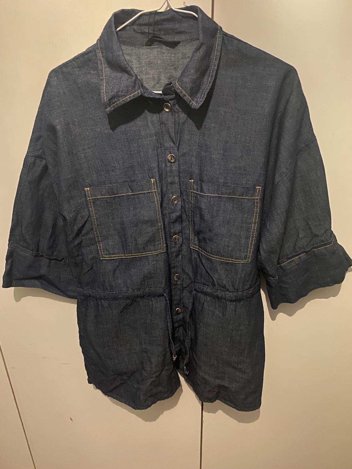 Dark blue denim shirt with front buttons and two large chest pockets, hanging on a white hanger.