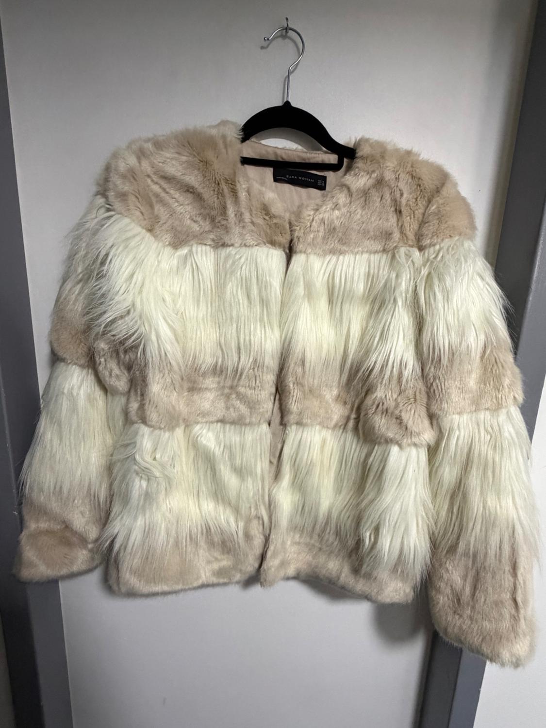 Faux leather jacket in beige and white tones hanging on a black hanger against a white wall.
