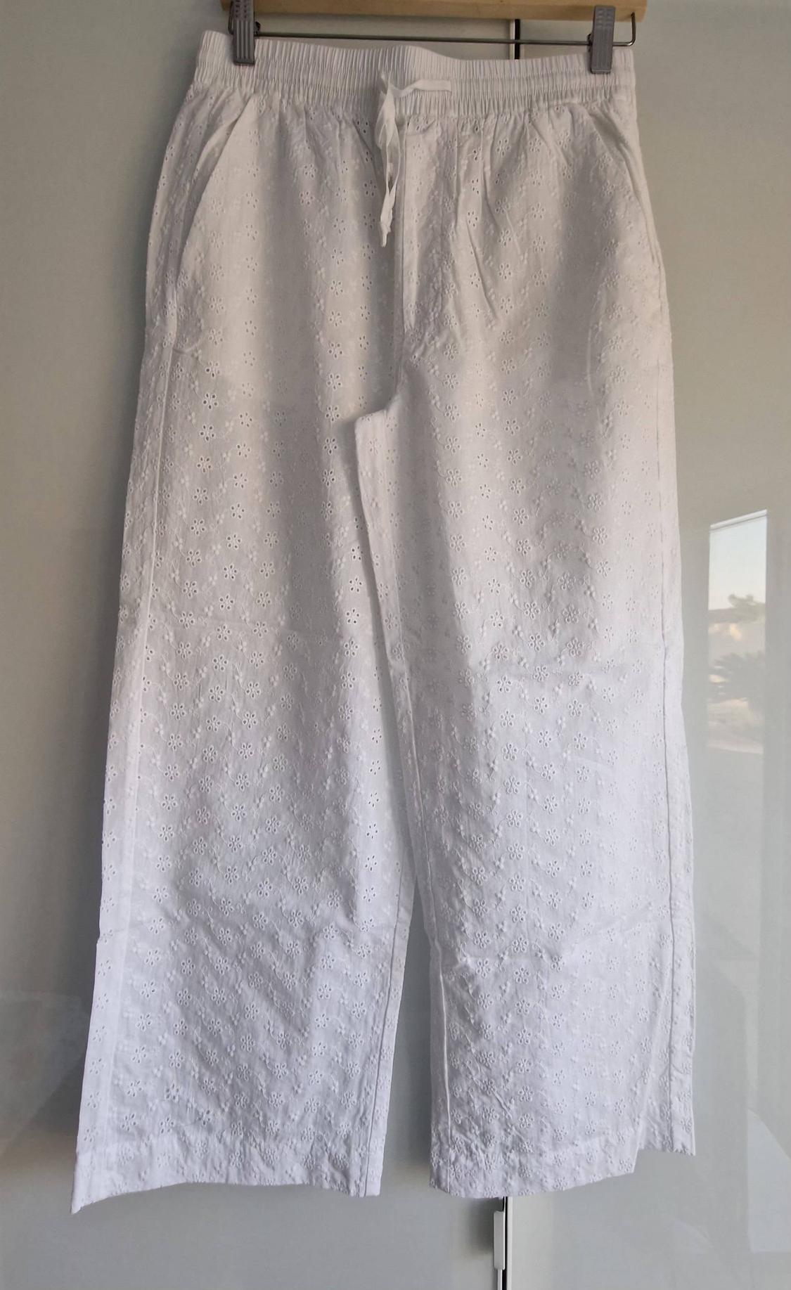 White trousers with an elasticated waist, drawstring and perforated floral embroidery, hanging on a hanger against a light background.