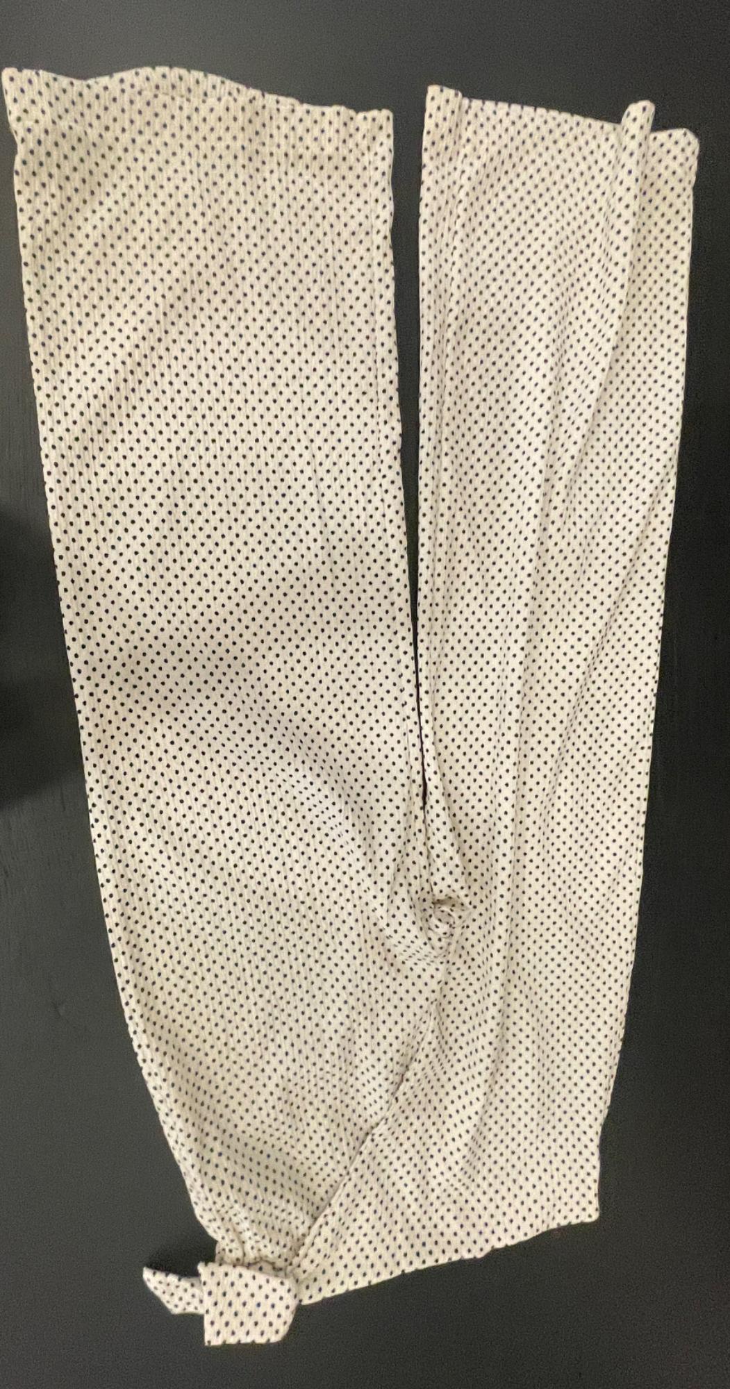 Light-coloured trousers with dark polka dots on a black background. The fabric has a crinkled texture and features a casual knot at the hem of one leg.