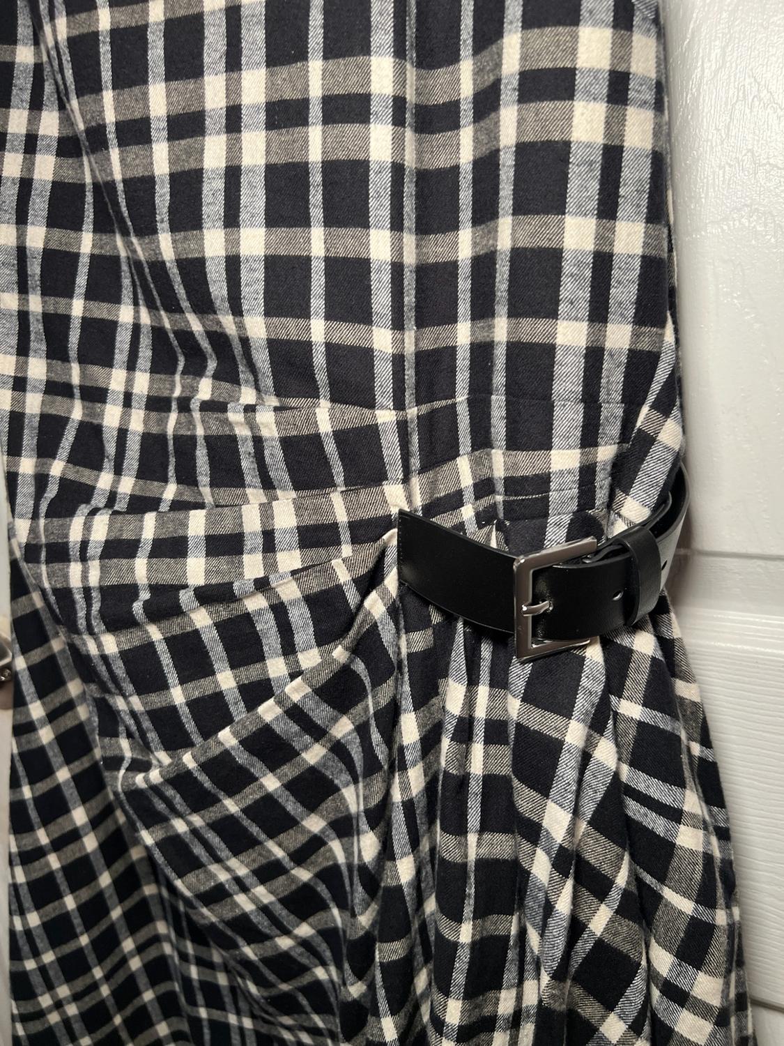 Detail of a garment with a black and white check print, gathered by a black belt with a silver buckle in front of a white door.