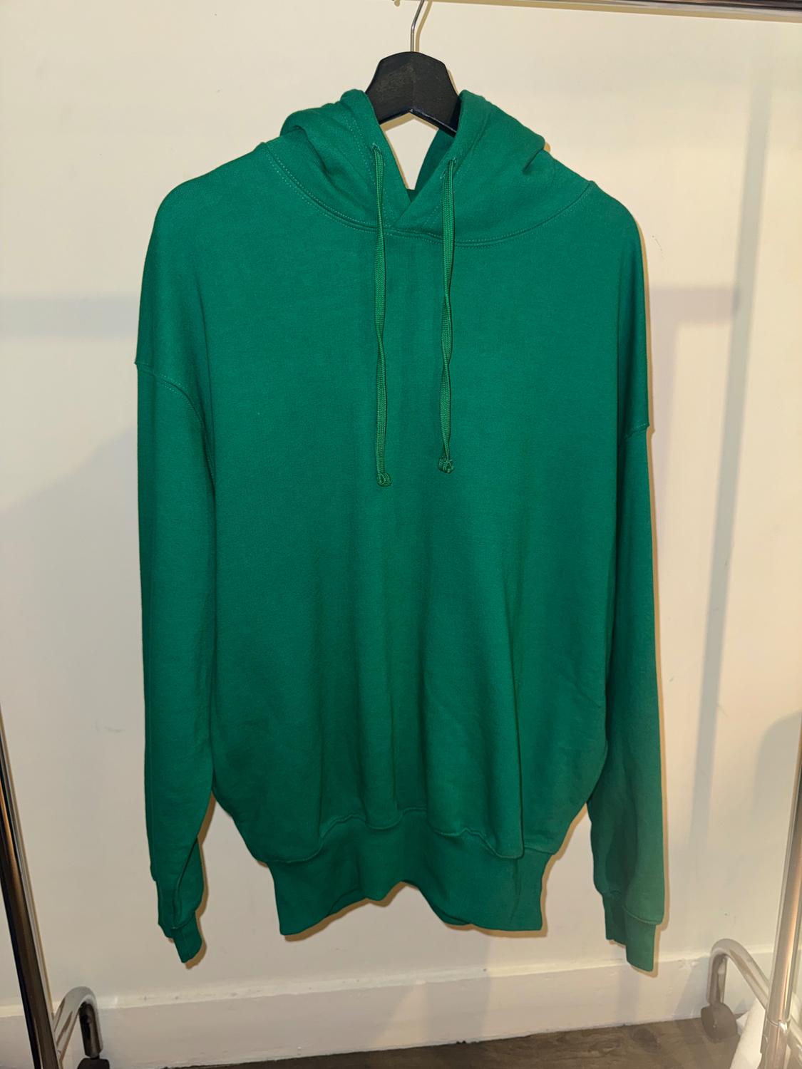 Green hooded sweatshirt with drawstrings, hanging on a black hanger, against a white background on a metal stand.