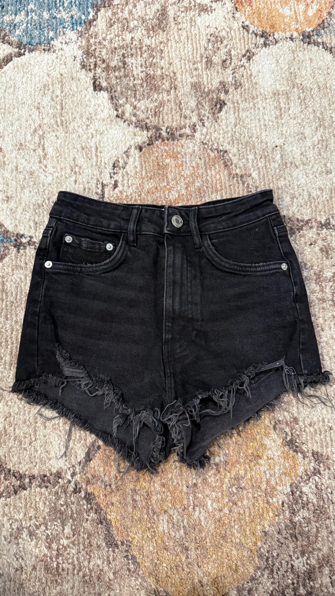 Black denim shorts with frayed edges on an abstract patterned rug in beige, blue, and orange tones.