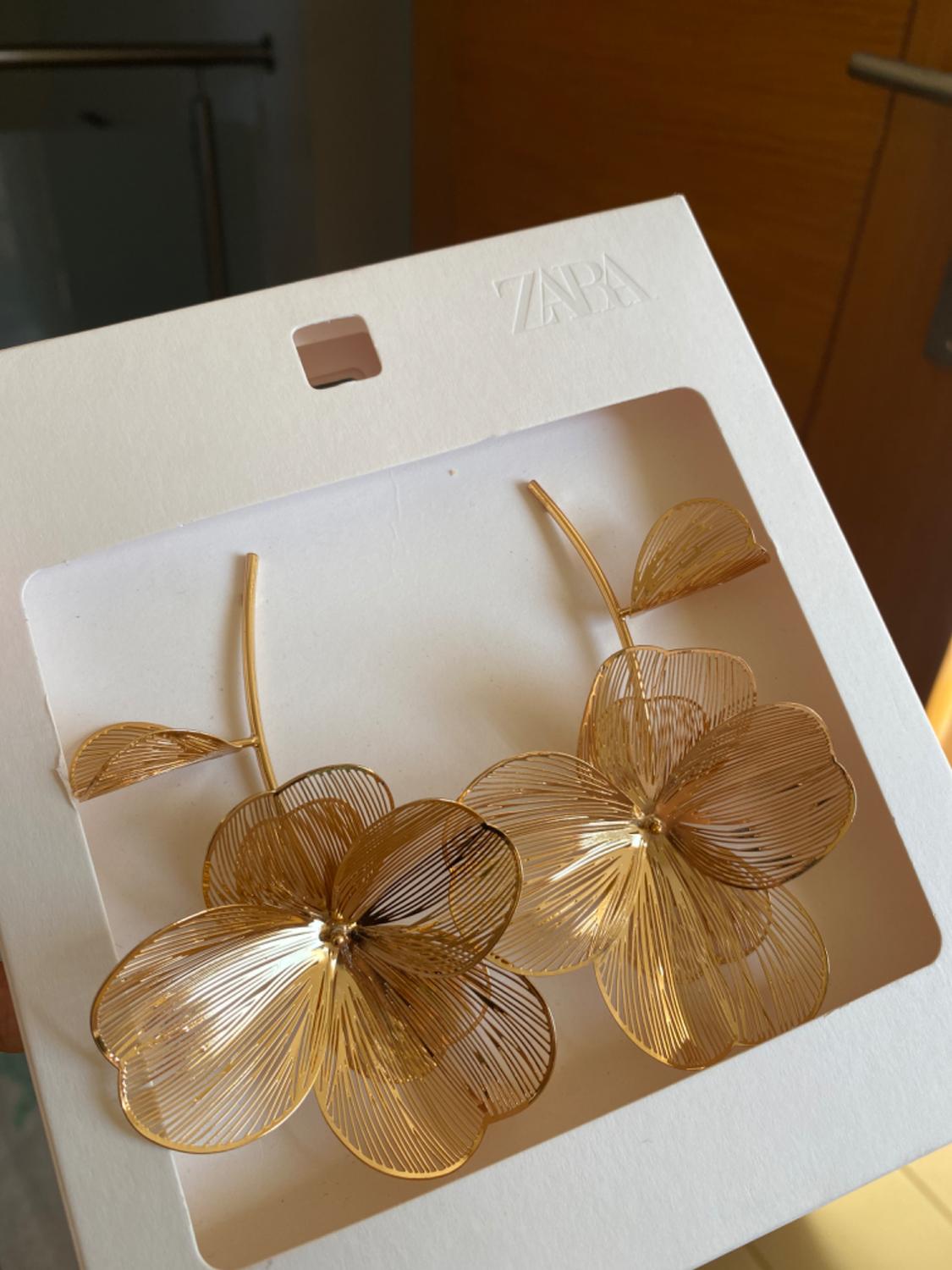 Gold-coloured flower-shaped earrings with a filigree design, presented in a white box with an embossed Zara logo.