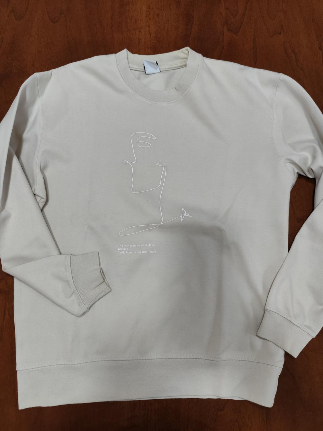 Beige sweatshirt with a minimalist line design of a face. Text: "The man with the poker face NODE 01 TYPE: Print on sweatshirt base".