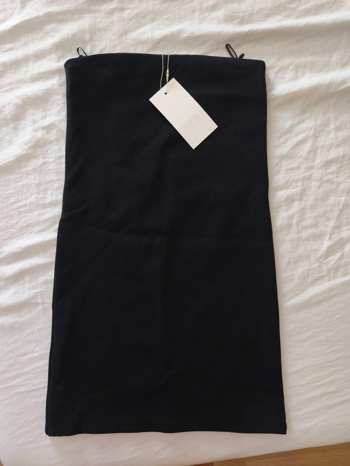Μαύρο στράπλες φόρεμα με λευκή ετικέτα ZARA, απλωμένο πάνω σε τσαλακωμένο λευκό σεντόνι.