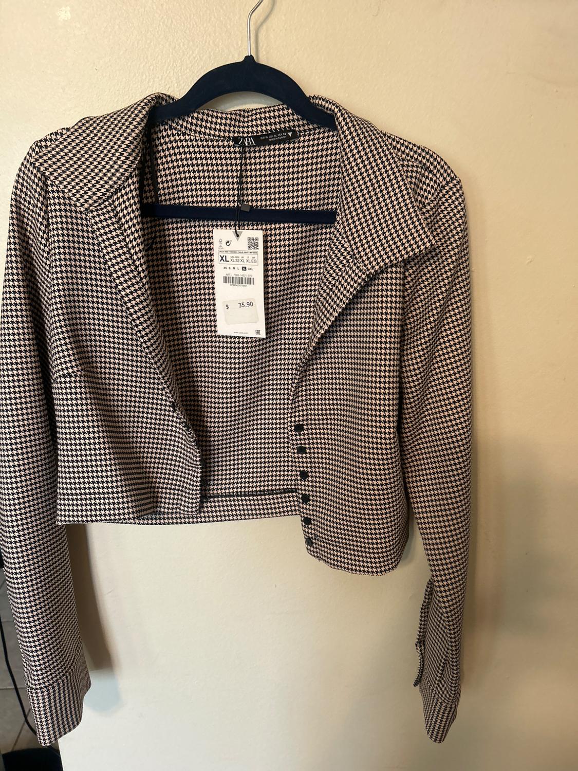 Short black and white checked jacket hanging on a black hanger. Label visible with price of $35.90 and size XL.