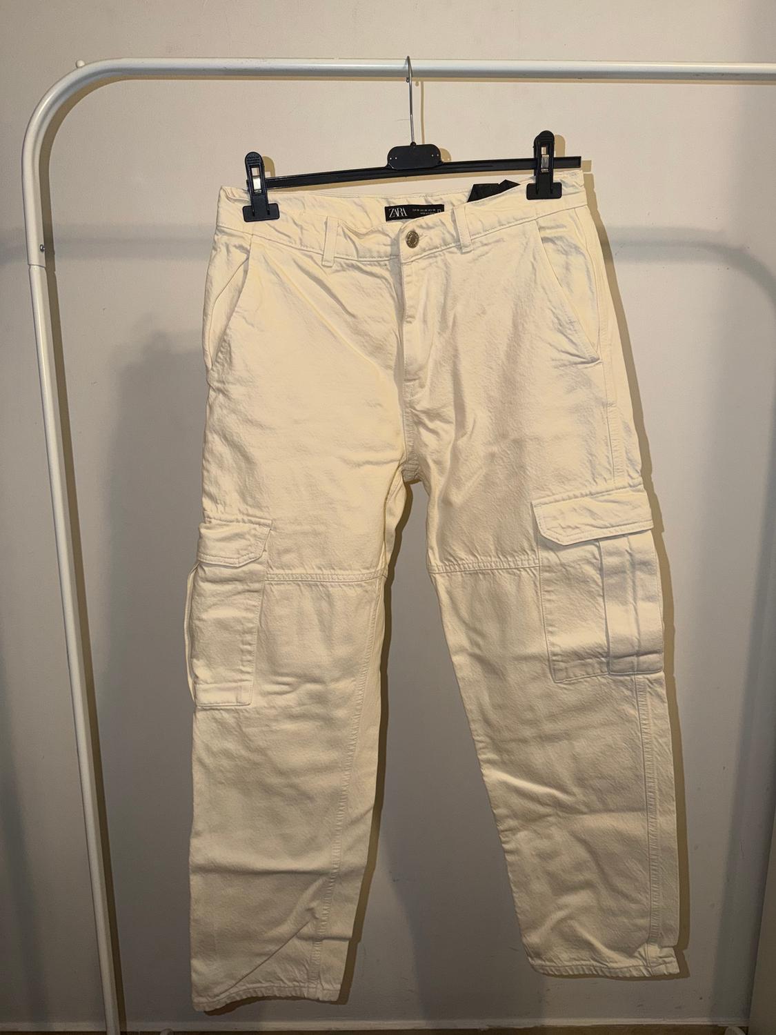 Beige cargo trousers hanging on a black hanger against a white background. Visible brand label on the waistband.