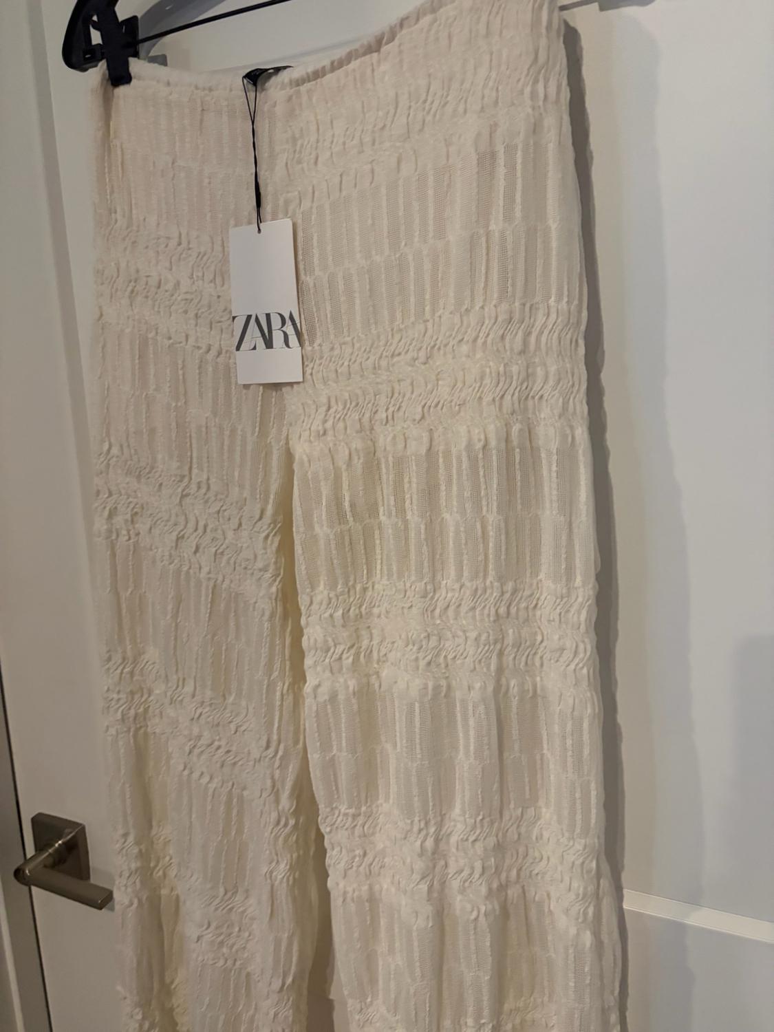 White textured trousers hanging on a door. Visible label with the text ZARA.