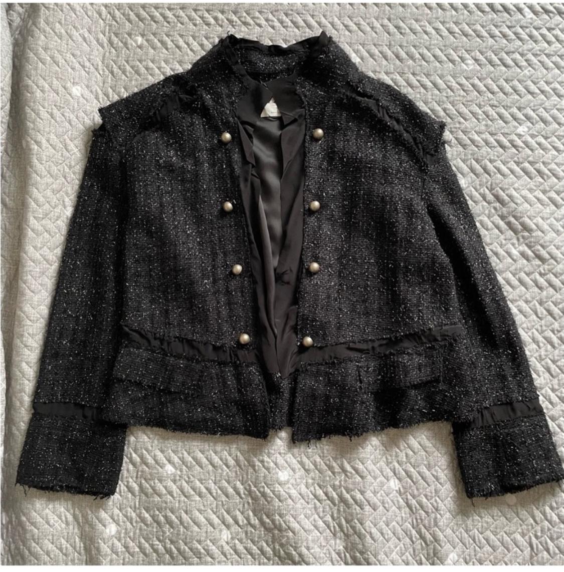 Black jacket with gold buttons on a gray geometric patterned quilt. The jacket has an elegant and textured design.