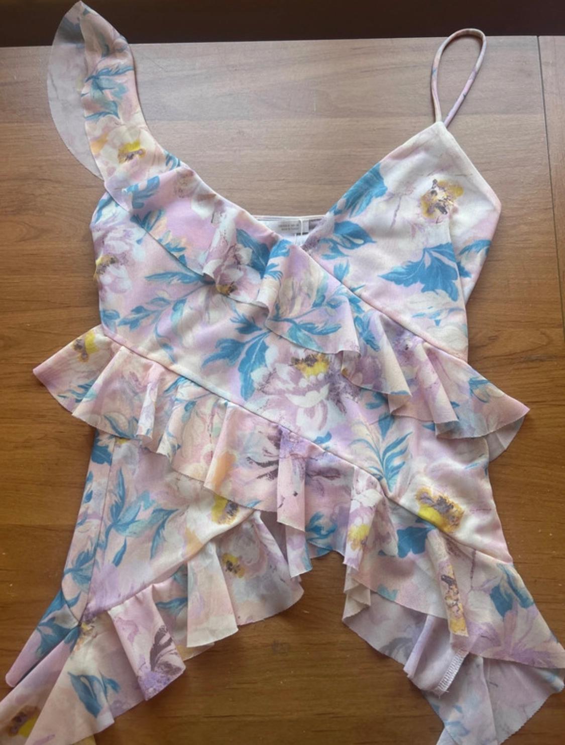 Pastel floral print camisole with asymmetric frills and a light wood background.